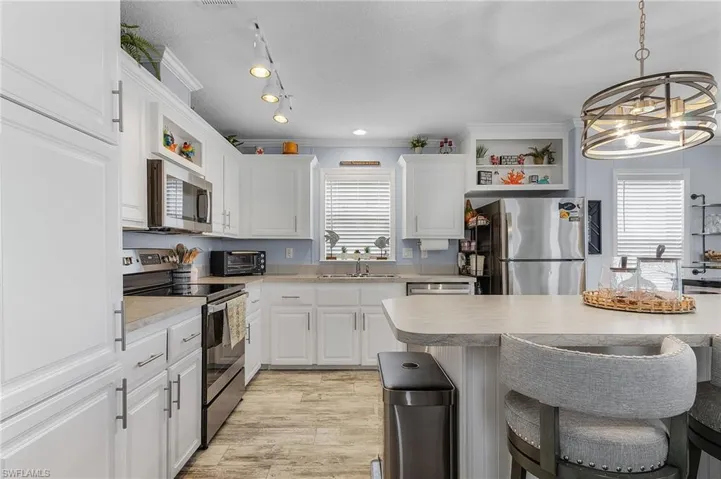 Kitchen with white cabinets, appliances with stainless steel finishes, a notable chandelier, light hardwood / wood-style floors, and a breakfast bar area