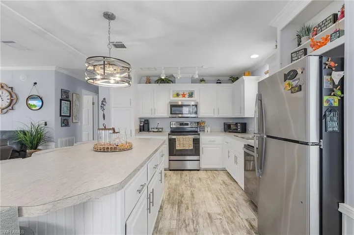 Kitchen with crown molding, hanging light fixtures, light wood-type flooring, white cabinetry, and stainless steel appliances