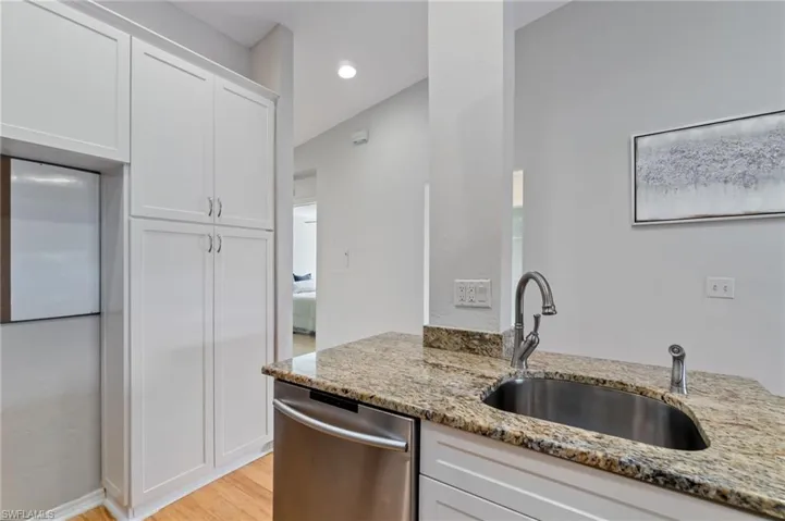 Kitchen featuring white cabinets, dishwasher, light wood-type flooring, light stone countertops, and recessed lighting