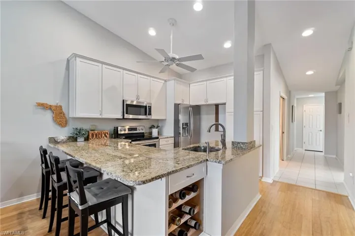 Kitchen featuring a wine rack, stainless steel appliances, light wood-style flooring, light stone countertops, and recessed lighting