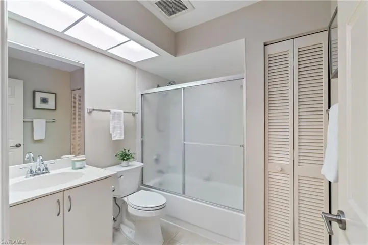 Full bath featuring a closet, vanity, shower / bath combination with glass door, and a skylight
