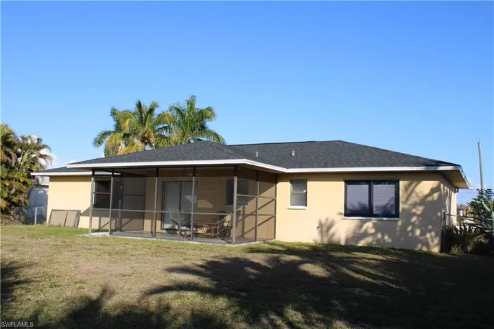 Rear view of house featuring stucco siding, a lawn, roof with shingles, and a sunroom