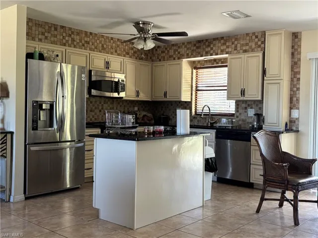 Kitchen featuring stainless steel appliances, cream cabinetry, a center island, decorative backsplash, and a ceiling fan