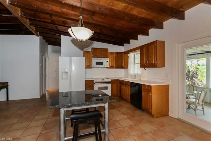 Kitchen with hanging light fixtures, sink, white appliances, and light tile flooring