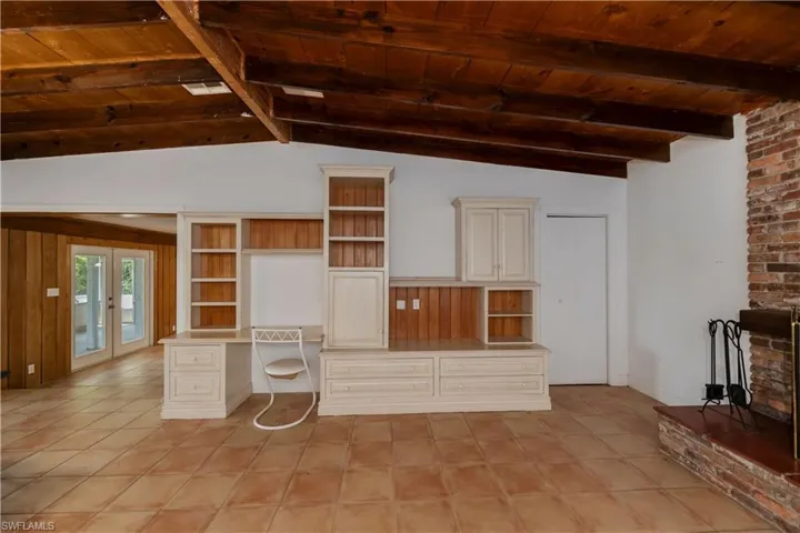 Unfurnished living room featuring french doors, brick wall, vaulted ceiling with beams, wooden ceiling, and light tile floors