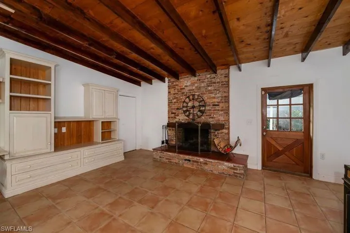 Unfurnished living room featuring beam ceiling, brick wall, a brick fireplace, and light tile floors