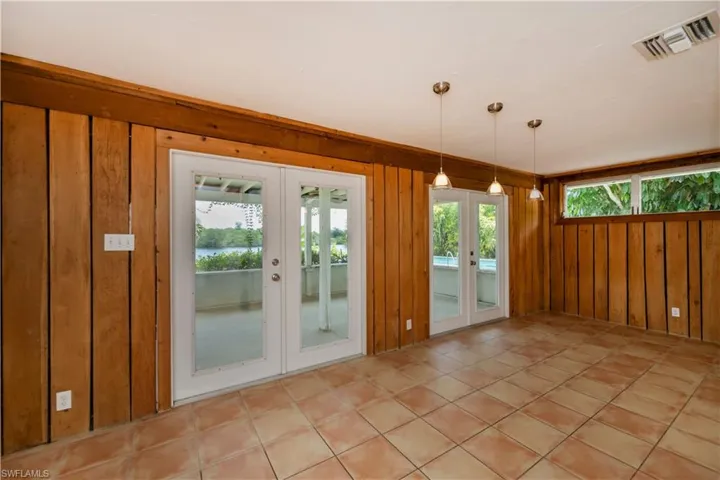Tiled empty room featuring french doors and wood walls
