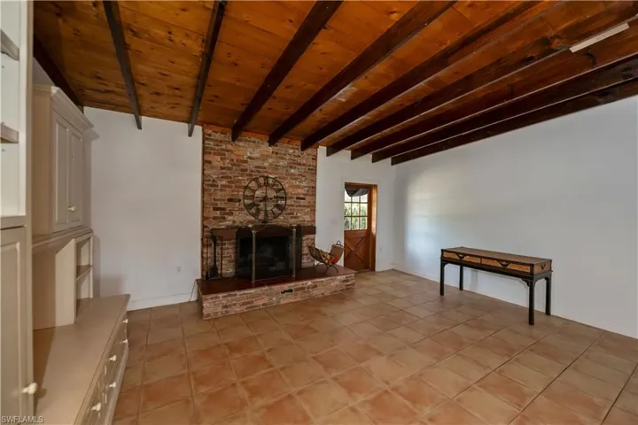 Unfurnished living room with brick wall, beamed ceiling, wooden ceiling, a brick fireplace, and light tile floors