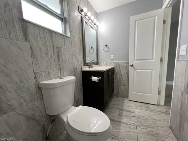 Bathroom with tile flooring, oversized vanity, tile walls, and toilet
