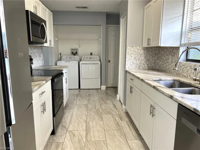 Kitchen with light stone counters, backsplash, white cabinetry, and appliances with stainless steel finishes