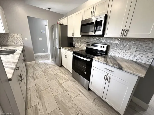 Kitchen featuring appliances with stainless steel finishes, white cabinets, backsplash, and light stone counters
