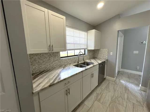 Kitchen featuring sink, dishwasher, white cabinets, and tasteful backsplash
