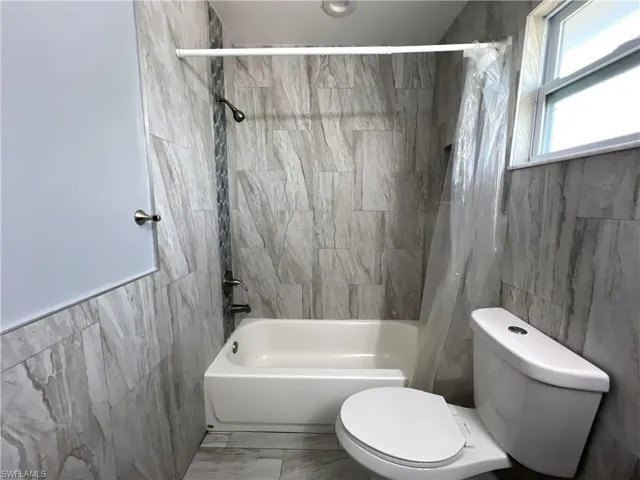 Bathroom with tile walls, tile flooring, shower / bath combo, and toilet