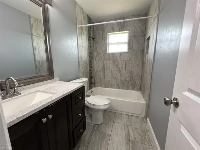 Full bathroom featuring tiled shower / bath, vanity, toilet, and tile flooring
