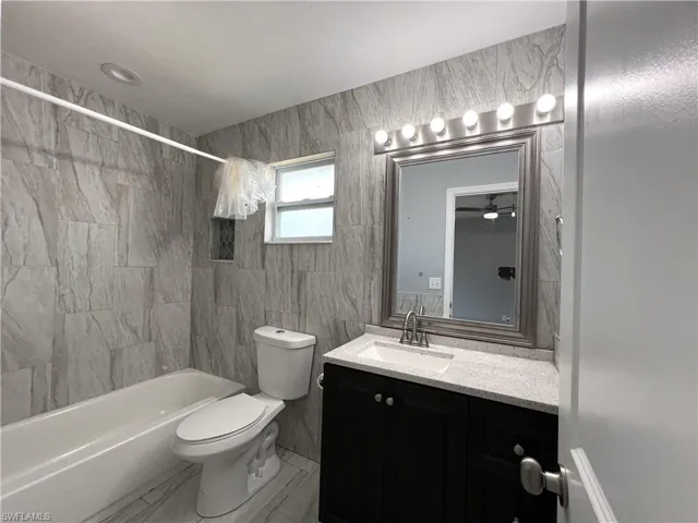 Full bathroom featuring tile walls, toilet, tile floors, tiled shower / bath combo, and vanity