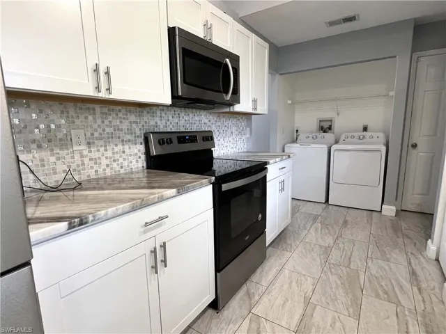 Kitchen featuring white cabinetry, appliances with stainless steel finishes, tasteful backsplash, and light tile flooring