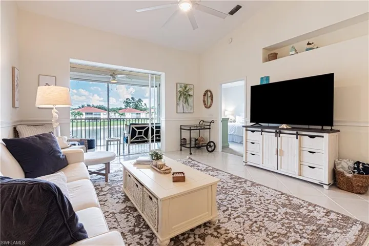Living room with ceiling fan, light tile patterned flooring, and high vaulted ceiling