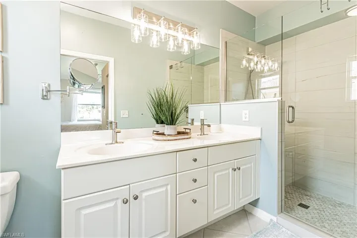 Ensuite bathroom with double vanity, tile patterned flooring, a shower stall, toilet, and a chandelier
