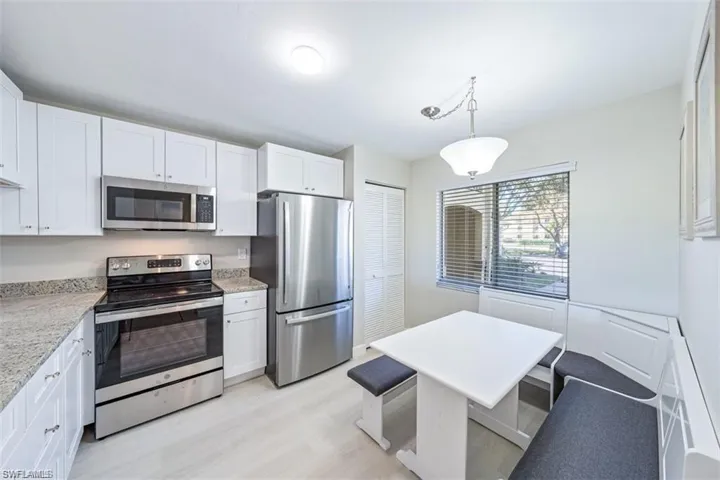Kitchen featuring stainless steel appliances, white cabinetry, light wood-style floors, and light stone counters