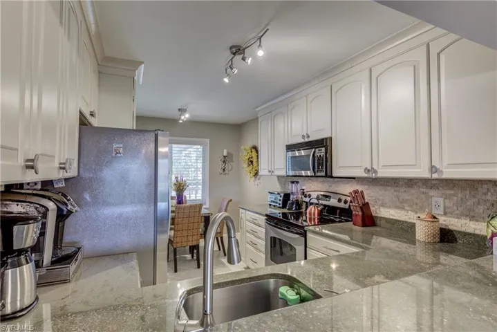 Kitchen featuring stainless steel appliances, white cabinetry, light stone counters, and decorative backsplash