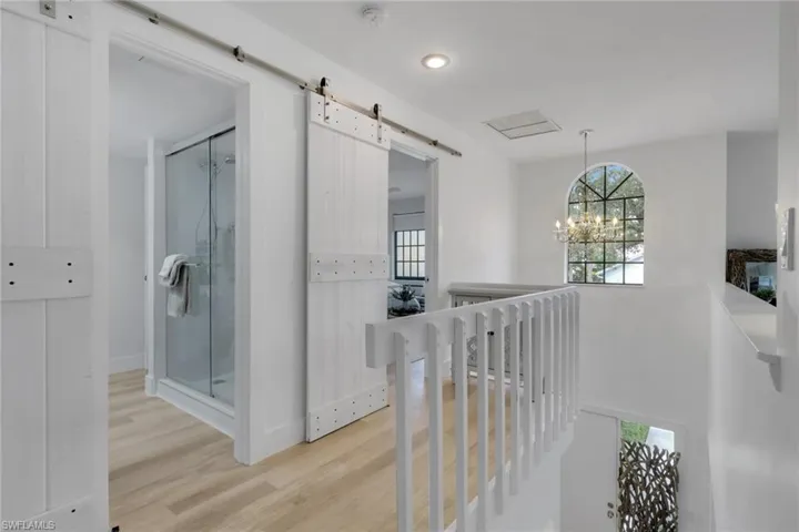 Corridor with light wood-style floors, healthy amount of natural light, a barn door, and a chandelier