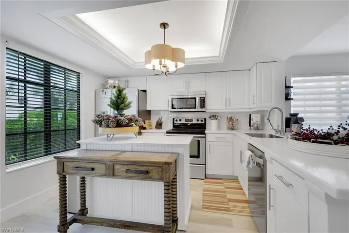 Kitchen featuring a raised ceiling, appliances with stainless steel finishes, white cabinetry, hanging light fixtures, and tasteful backsplash