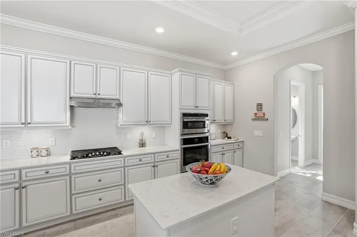 Kitchen with arched walkways, a center island, light stone counters, white cabinets, and backsplash