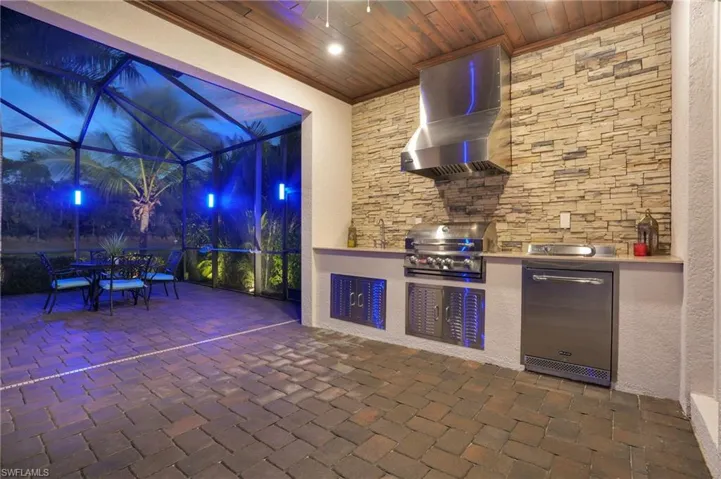 Patio at night with a lanai, a patio, exterior kitchen, outdoor dining space, and a sunroom