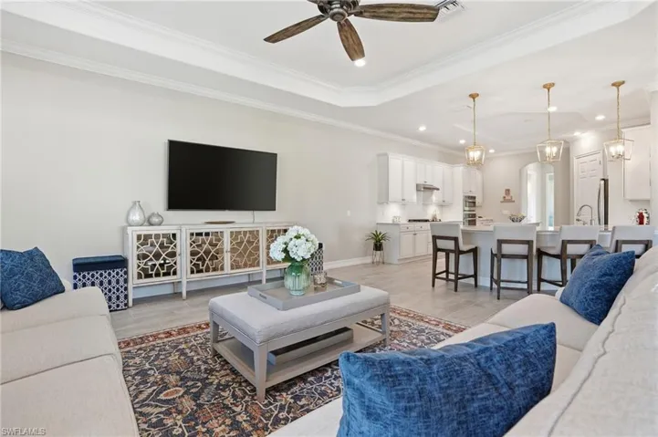 Living room with ornamental molding, a ceiling fan, a chandelier, a raised ceiling, and arched walkways