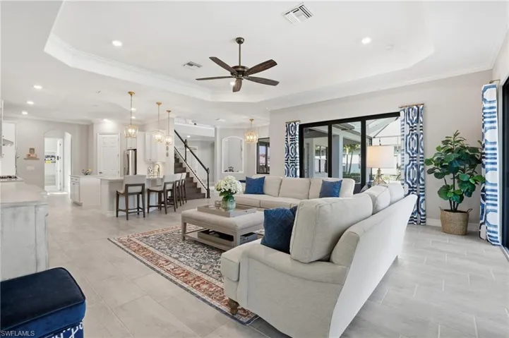 Living area with a tray ceiling, ornamental molding, arched walkways, a chandelier, and ceiling fan