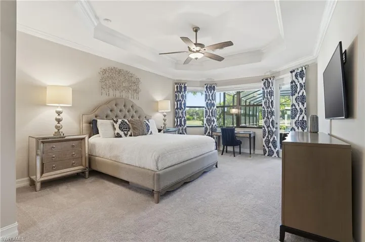 Bedroom featuring an office area, crown molding, a ceiling fan, light carpet, and a tray ceiling
