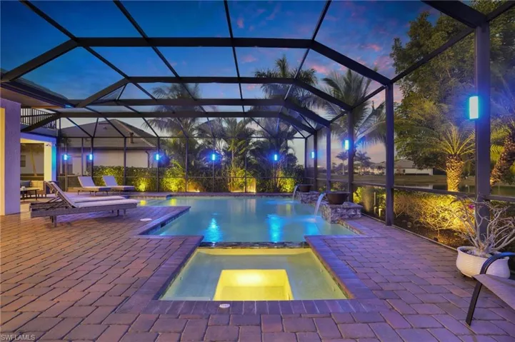 View of pool featuring glass enclosure, a pool with connected hot tub, a sunroom, and a patio area