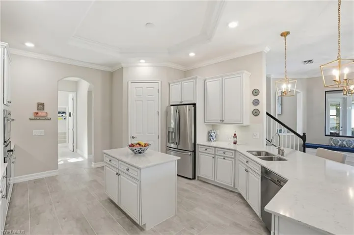 Kitchen with white cabinetry, stainless steel appliances, decorative light fixtures, a center island, and crown molding