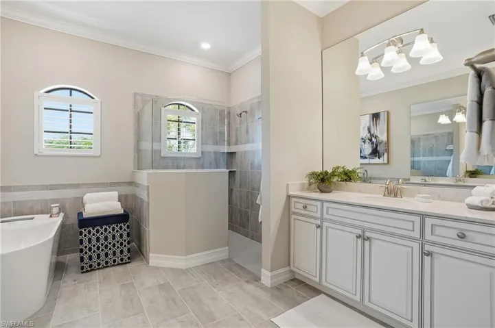 Bathroom featuring walk in shower, vanity, a freestanding bath, crown molding, and tile walls