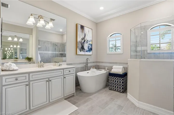 Bathroom with tiled shower, a freestanding bath, vanity, crown molding, and a wainscoted wall
