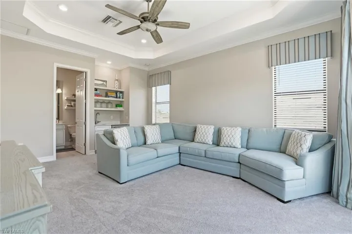 Living room featuring a raised ceiling, carpet, crown molding, a ceiling fan, and recessed lighting