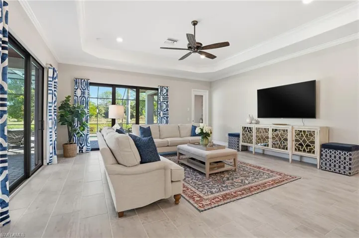 Living area featuring a tray ceiling, ornamental molding, light wood-style flooring, and ceiling fan