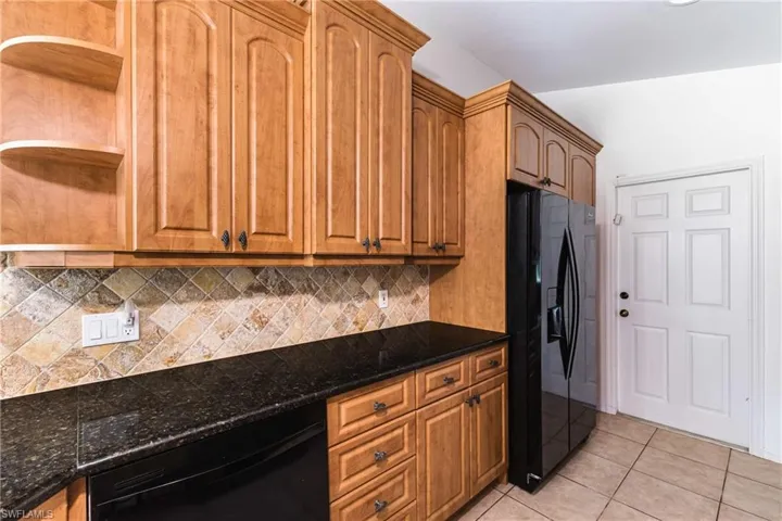 Kitchen featuring black appliances, open shelves, light tile patterned flooring, dark stone countertops, and wood finish cabinetry