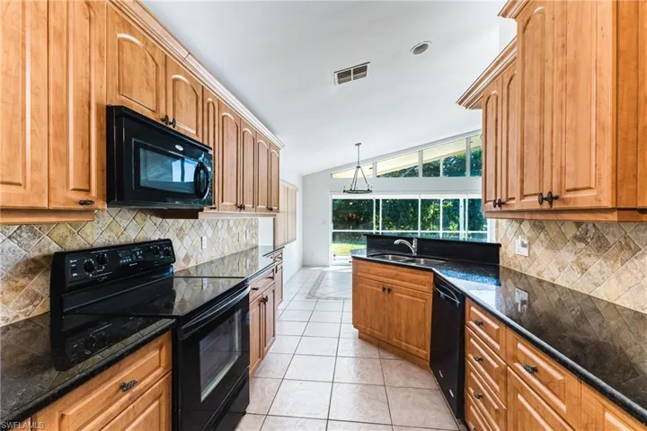 Kitchen with black appliances, light tile patterned floors, lofted ceiling, wood finish cabinetry, and dark stone counters