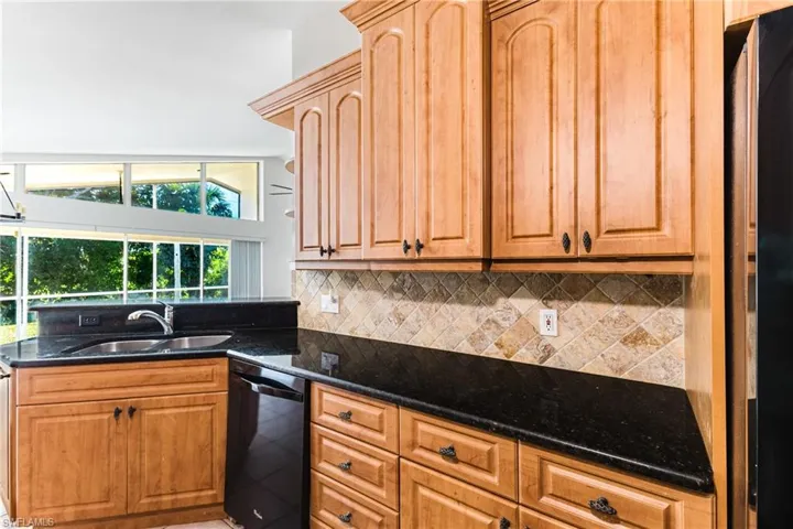 Kitchen with dark stone counters, black appliances, a peninsula, and backsplash