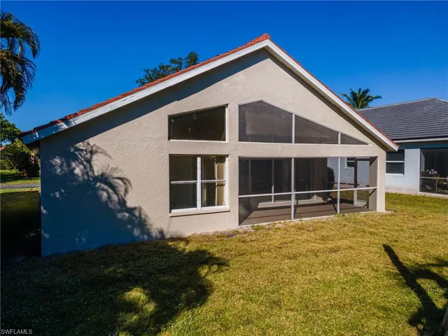 Rear view of house featuring a lawn, stucco siding, and a sunroom