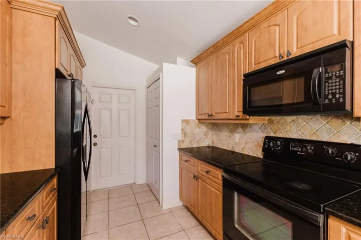 Kitchen featuring black appliances, dark stone counters, light tile patterned floors, lofted ceiling, and backsplash