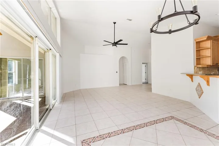 Unfurnished living room with light tile patterned floors, arched walkways, a ceiling fan, hanging lights, and vaulted ceiling