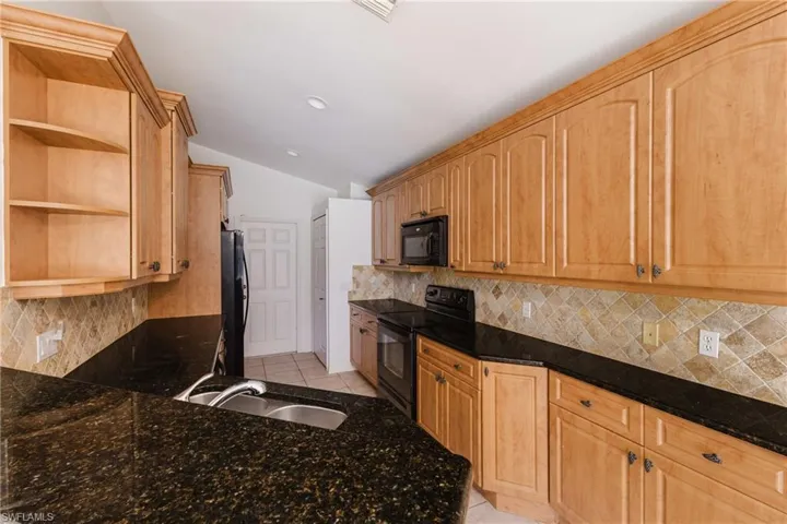 Kitchen featuring open shelves, black appliances, light tile patterned floors, vaulted ceiling, and dark stone counters