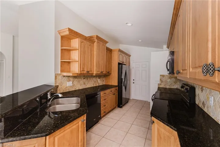 Kitchen featuring open shelves, dark stone countertops, black appliances, light tile patterned floors, and light wood finish cabinetry