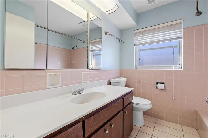 Bathroom with tile walls, plenty of natural light, toilet, and tile patterned flooring