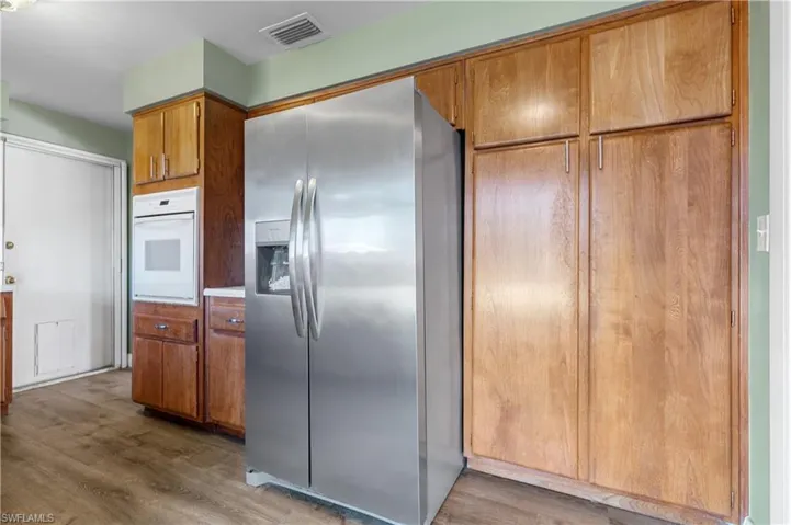 Kitchen featuring brown cabinets, stainless steel fridge, wood finished floors, visible vents, and white oven