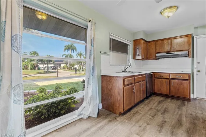 Kitchen featuring brown cabinets, dishwasher, light countertops, wood finished floors, and under cabinet range hood
