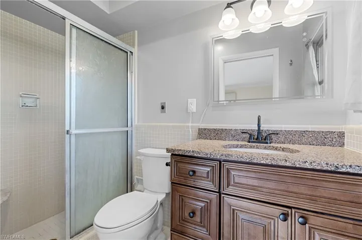 Bathroom with toilet, tile walls, a shower stall, and vanity