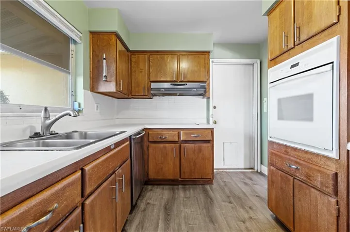 Kitchen with brown cabinetry, range hood, wood finished floors, a sink, and oven